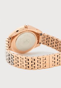 Ρολόι χειρός σε ροζ χρυσό με μεταλλικό συνδεδεμένο μπράσελετ, λαμπερούς κρυστάλλους στο βραχιολάκι και στρογγυλή πίσω θήκη με ορατές χαραγμένες λεπτομέρειες.