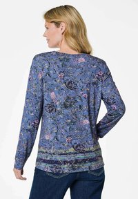 Langarmoberteil aus blauer Stoff mit floralem und paisleymuster, rundem Ausschnitt und Schlitzen am Saum für mehr Bewegungsfreiheit.