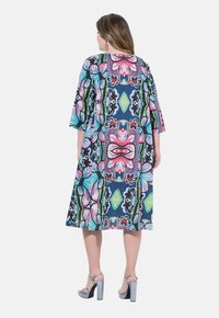 Vestido impreso de corte holgado, con mangas tres cuartos, que presenta un colorido estampado floral sobre un fondo marino. La longitud llega hasta la mitad de la pantorrilla.