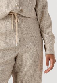 Beige textuuroutfit met een subtiel visgraatpatroon, voorzien van sprankelende accenten, een koordjesband en knoopdetails op de top.
