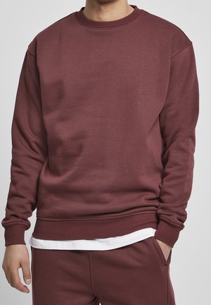 Person iført en ensfarvet vinrød sweatshirt og matchende bukser, med en hvid skjorte, der kigger frem under.