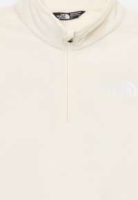 Pullover in pile color crema, con apertura a metà zip sul davanti, colletto alto e logo bianco ricamato sul petto. Texture morbida, design casual.