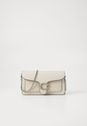 Bolso de hombro de cuero beige con una correa de cadena plateada, que presenta un cierre circular decorativo adornado con piedras transparentes y bordes redondeados.