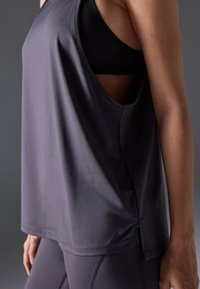 Sleeveless dark gray tank top with a relaxed fit, soft texture, featuring a side cutout design and a small logo near the hem.