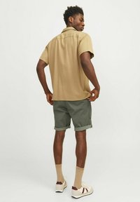 Chemise à manches courtes beige, coupe décontractée, associée à un short vert. Le short est retroussé au niveau de l'ourlet. Les chaussures sont crème avec des accents bordeaux.