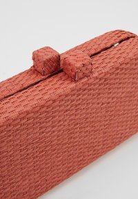 Pochette tissée rectangulaire couleur terre cuite avec deux fermoirs tissés arrondis sur le dessus sur un fond uni.