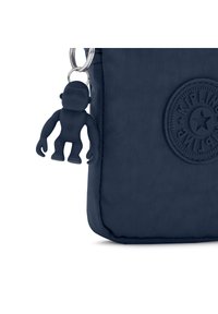 Borsa in tessuto blu navy con una superficie testurizzata e un logo rotondo. È attaccato un portachiavi in gomma blu scuro a forma di scimmia.
