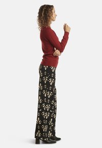 Red sweater and black patterned wide-leg pants, featuring cream floral motifs, paired with black heeled boots. Texture appears soft and smooth.