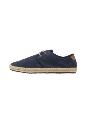 Zapato espadrille azul marino con parte superior de lona texturizada, suela de cuerda de yute natural y acento de cuero marrón en el talón. Presenta un diseño de cordones.