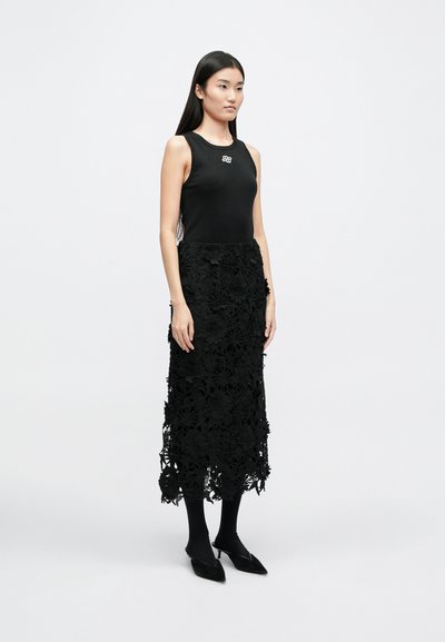 Fekete ruha, amely illeszkedő bordázott felső résszel és hosszú csipkés szoknyával rendelkezik, virágmintázatú kivágásokkal. Fekete harisnyával és hegyes orrú balerinacipővel viselve. Ezüst logó részlet.