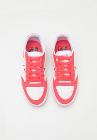 Piros és fehér sneaker, texturált felsőrésszel, kerek fűzőkkel és megerősített orr résszel. Lapos fehér talp logóval a nyelvén.