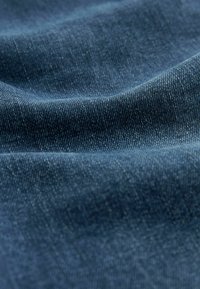 Close-up van donkerblauwe denimstof met zichtbare textuur en weefpatroon, met zachte plooien en kreukels.