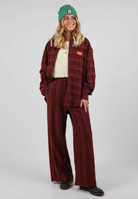 Veste surdimensionnée à motif rouge et noir et pantalon évasé, avec une coupe décontractée et une poche poitrine. Associée à un bonnet vert.