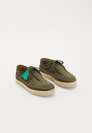 Green lace-up shoes with textured upper, smooth suede accents, brown leather lining, and woven jute soles. Features a green tag detail.