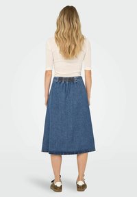 Denim A-line krilo z nabranim, elastičnim pasom, neobdelanim robom in dolžino do kolen, v kombinaciji z oprijetim kremastim zgornjim delom ter prostorno obutvijo.