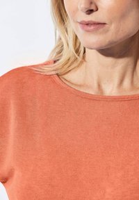 Oranje gebreide top met een ronde halslijn, een gladde textuur en korte mouwen. De stof lijkt zacht, lichtgewicht en casual.