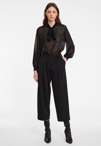 Zwarte doorschijnende blouse met een strik hals en lange mouwen, gecombineerd met hoge zwarte pinstripe wijde broek. Zwarte enkellaarsjes.