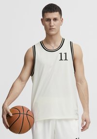 Hvit basketball-drakt med svarte detaljer og nummer 11. Mesh-stoffet har et teksturert mønster, sammen med en basketball i hånden.