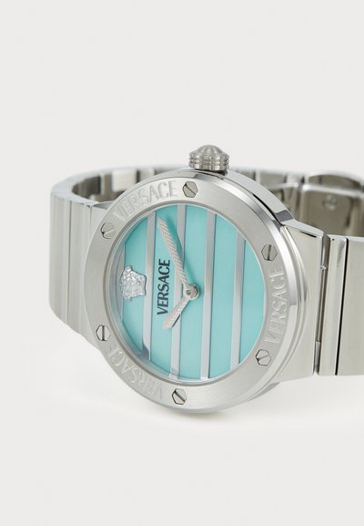 Ασημένιο ρολόι από ανοξείδωτο ατσάλι με φωτεινό μπλε σχέδιο λωρίδων στον καντράν, που διαθέτει λογότυπο, δίχρωμες δείκτες και κορώνα. Περιλαμβάνει μεταλλικό βραχιόλι.