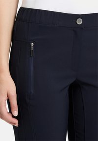 Tengerészkék nadrág rugalmas derékkal, oldalán cipzáras zsebbel és sima szövettextúrával. Kényelemre és funkcionalitásra tervezve.