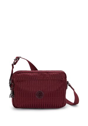 Red fabric crossbody bag with a textured pattern, zip closure, adjustable strap, and logo detail on the front. Compact rectangular shape.