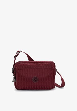 Borsa a tracolla rossa in tessuto con motivo testurizzato, chiusura a zip, tracolla regolabile e dettagli logo sul davanti. Forma rettangolare compatta.