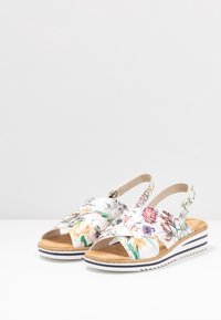 Blommönstrade sandaler med ljus bakgrund, korsremdesign, slingback, vadderad innersula och texturerad kilklack med kontrasterande ränder.