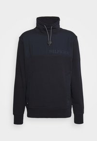 Sudadera azul marino con cuello alto, cremallera, bolsillos frontales y texto con el logo en el pecho. Tejido suave y corte holgado.