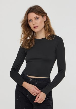 Czarny krótki top z długim rękawem i okrągłym dekoltem, wykonany z gładkiego, elastycznego materiału, zestawiony z ciemnymi dżinsami z delikatnymi zdobieniami.