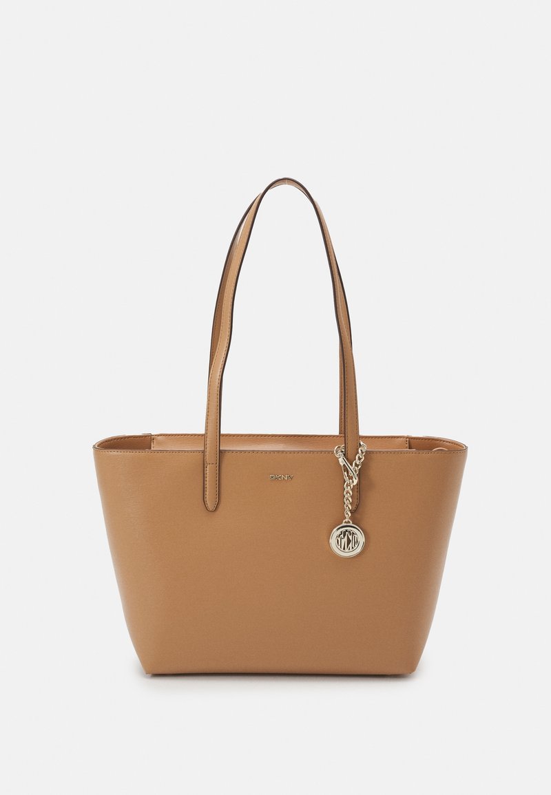 Sac cabas en cuir fauve avec double anse épaule et breloque logo circulaire dorée, marque embossée au centre devant.