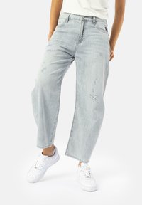 Jeans in denim blu chiaro, con effetto usurato, vestibilità rilassata, gambe dritte, design a cinque tasche e orli sfrangiati, abbinati a sneakers bianche.
