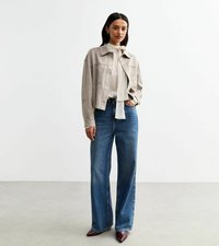 Lichtgrijze cropped jas, witte blouse met strik, wijde blauwe jeans en bordeauxrode hakken, geplaatst tegen een plain achtergrond.