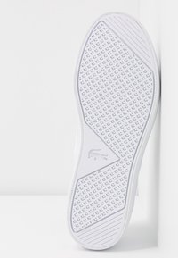 Semelle de basket blanche avec un motif texturé en forme de losange et un logo de crocodile intégré, photographiée sur un fond blanc.