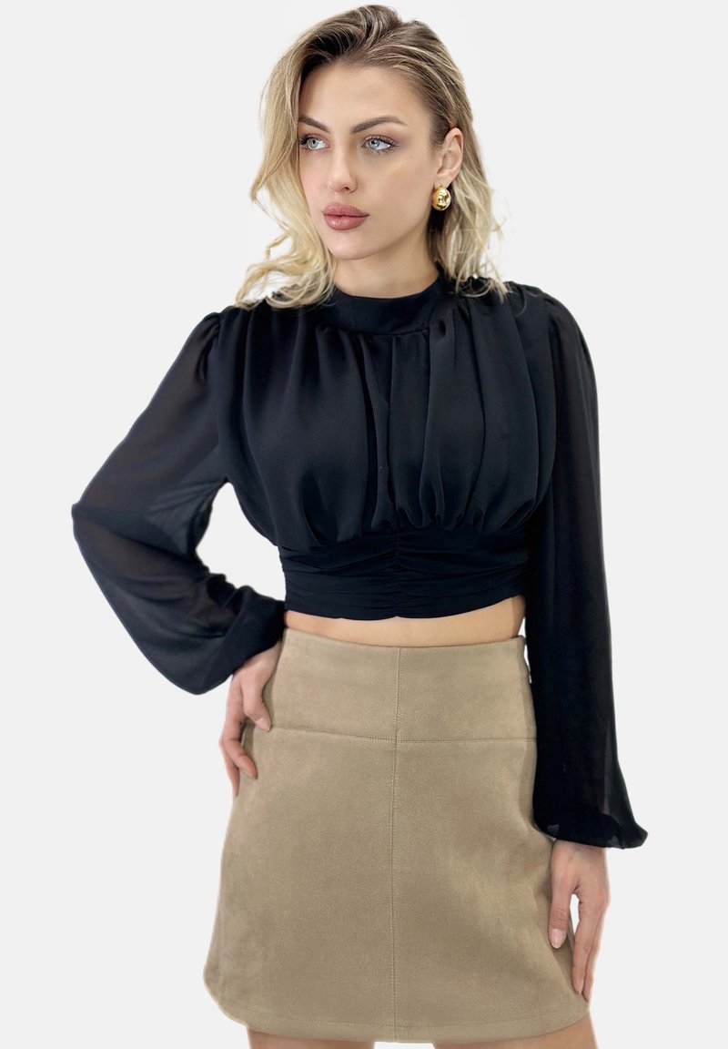Blusa nera cropped con maniche a sbuffo, caratterizzata da pieghe sul davanti. Abbinata a una mini gonna in pelle scamosciata color carne con dettagli sulle cuciture.