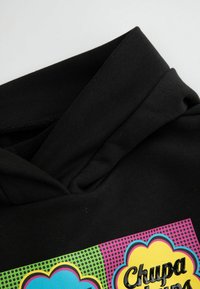 Czarna bluza z kapturem z kolorowym nadrukiem graficznym, na którym znajdują się kształty chmur w kolorze żółtym, niebieskim i różowym oraz tekst "Chupa Chups", o teksturowanym wzorze.
