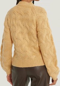 Pull en tricot torsadé de couleur jaune pâle, avec un col haut, un motif texturé et un ourlet côtelé. Les manches sont volumineuses, ce qui accroît la chaleur.