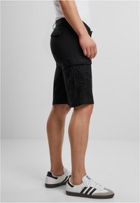 Shorts cargo noirs avec plusieurs poches, coupe jusqu'aux genoux, en tissu de coton. Associés à des baskets blanches avec des accents noirs et gris.