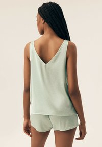 Jasnozielony zestaw piżamowy z bezrękawową bluzką i szortami. Tkanina ma subtelny teksturę z małymi białymi kropkami. Projekt w kształcie litery V.