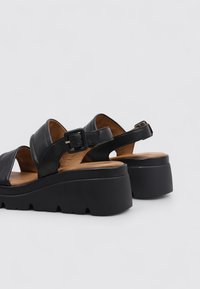 Sandalias de cuero negro con plataforma baja, que cuentan con tiras anchas y cierre de hebilla, plantilla texturizada y suela contorneada.