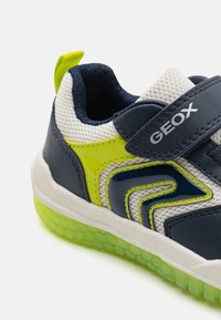 Sneaker with a navy leather upper, mesh panels, green accents, white sole, and a textured, translucent green outsole. Velcro strap included.