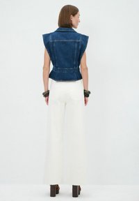 Gilet di jeans senza maniche con dettagli sulle spalle, vita stretta e tasche posteriori. Abbinato a pantaloni bianchi a gamba larga e tacchi alti marroni.