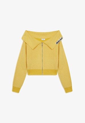 Žlutý zkrácený kardigan s naddimenzovaným límcem, strukturovanou tkaninou, předním zipem a štítkem na límci. Hladká, lehká konstrukce.