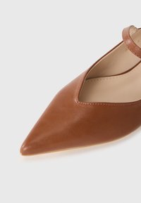 Bruin puntige schoen gemaakt van glad leer met een uitsnijdontwerp en een dunne enkelband. Bevat een lichtgekleurde binnenzool en een smalle hak.