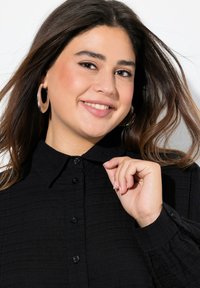 Black button-up shirt with a textured fabric, featuring a collared neck and long sleeves, shown with a close-up of the neckline and buttons.