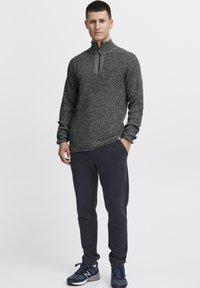 Strukturierter, dunkelgrauer Halbzip-Pullover mit langen Ärmeln, kombiniert mit marineblauen Jogginghosen. Das Modell trägt marineblaue Laufschuhe. Einfaches, lässiges Design.