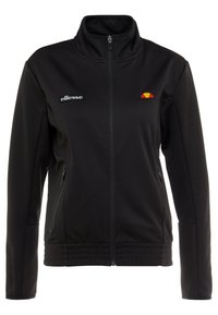 Schwarze Softshelljacke mit hohem Kragen, seitlichen Reißverschlusstaschen und elastischen Bündchen. Eigenschaften eines kleinen roten und gelben Logos auf der linken Brust.