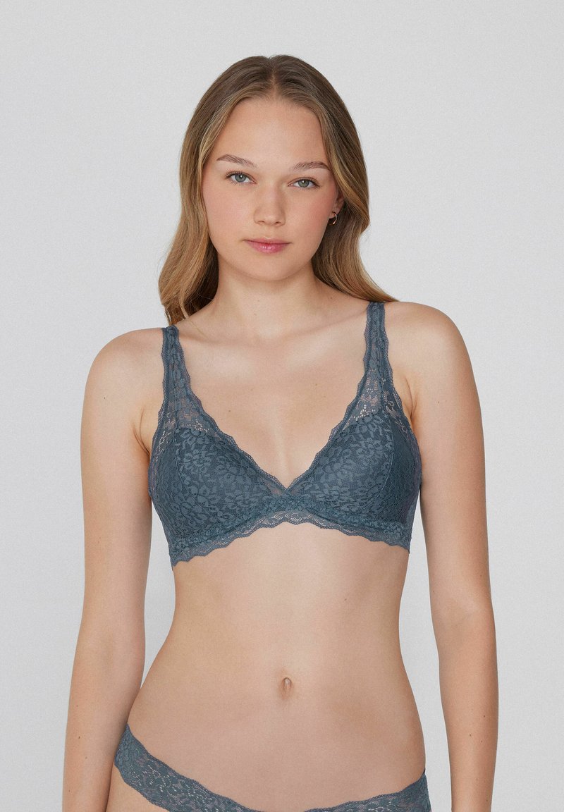 Bralette de encaje en color verde azulado apagado con escote en V, bordes festoneados y patrones florales intrincados. Tirantes ajustables para un ajuste personalizado.