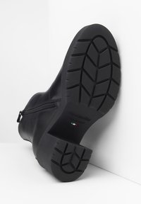 Black leather ankle boot with a side zipper, textured rubber sole featuring a tread pattern, and embossed branding on the heel.
