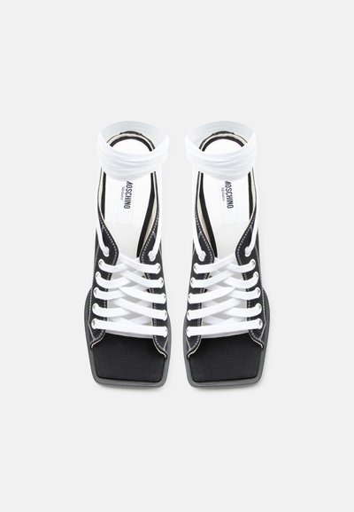 Sandales à talons hauts ouvertes à l'avant, noires et blanches, avec un devant carré, des lacets blancs et des brides à la cheville, étiquetées Moschino Milano à l'intérieur.