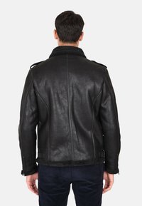 Giacca in pelle nera con colletto in shearling, finitura texturizzata e design aderente. Presenta cerniere e un interno liscio.
